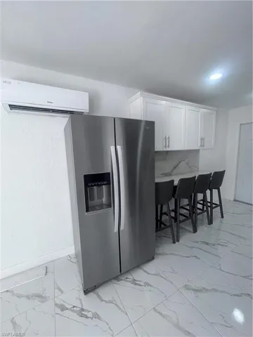 Kitchen featuring stainless steel fridge, white cabinetry, a breakfast bar, light marble finish floors, and backsplash