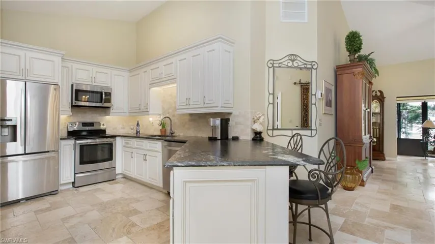 Kitchen with white cabinetry, stainless steel appliances, sink, kitchen peninsula, and high vaulted ceiling