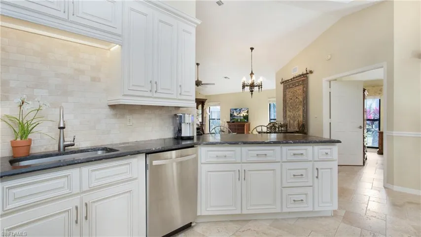 Kitchen with sink, white cabinetry, dishwasher, and lofted ceiling