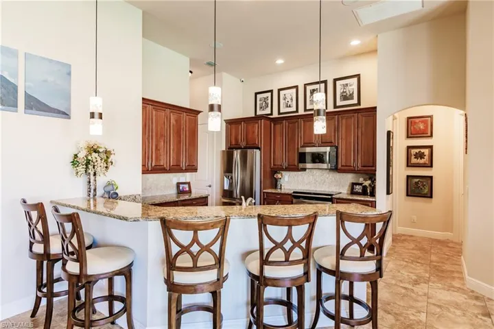 Kitchen featuring light granite countertops, appliances with stainless steel finishes, decorative light fixtures, and kitchen peninsula