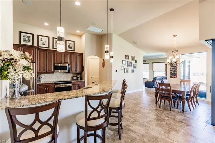 Kitchen featuring appliances with stainless steel finishes, a breakfast bar, hanging light fixtures, and light granite countertops