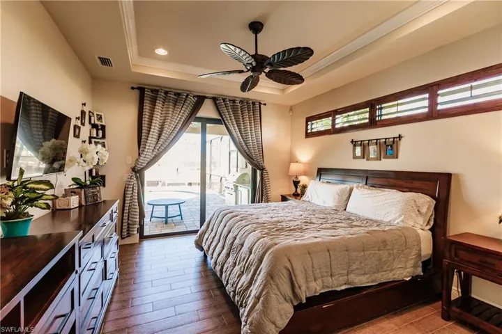 Primary bedroom featuring wood-style flooring, ornamental molding, a raised ceiling, and access to outside