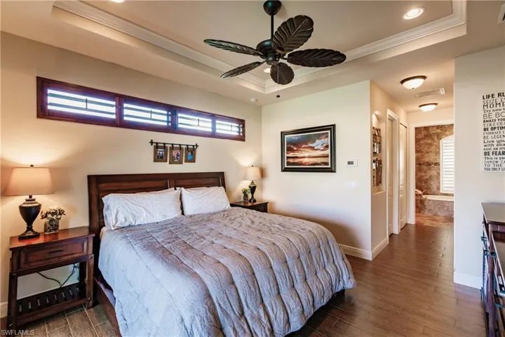 Primary bedroom with crown molding wood-style floors, ceiling fan, and a tray ceiling