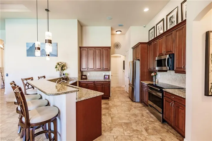 Kitchen with pendant lighting, a kitchen bar, kitchen peninsula, stainless steel appliances, and light granite countertops
