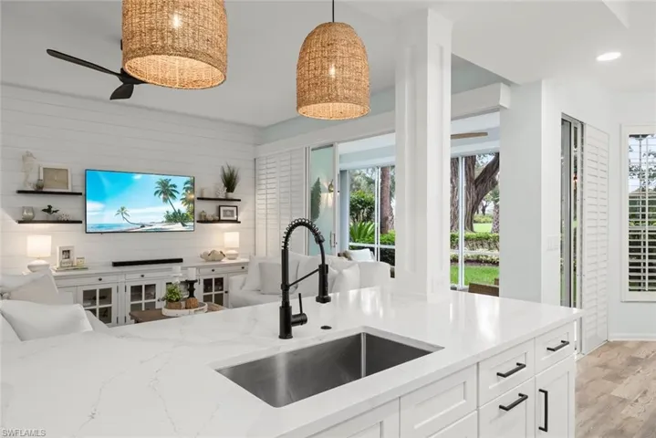 Kitchen island with quartz countertop, undermount stainless steel sink, matte black gooseneck faucet, and pendent lights.