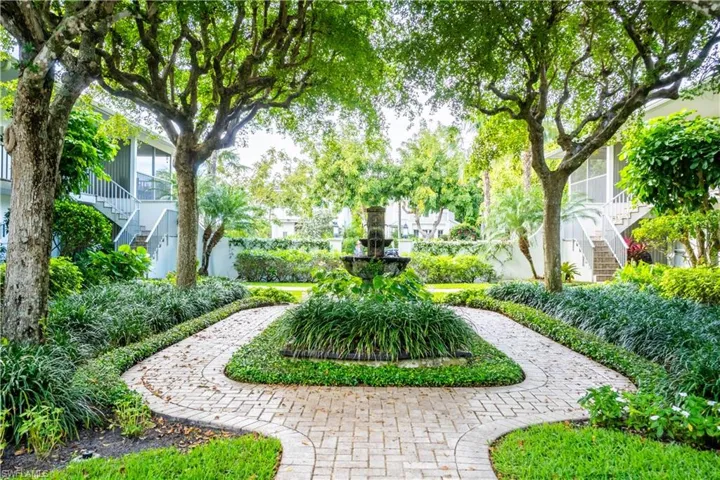 Beautifully landscaped grounds featuring mature trees, lush green foliage, and a decorative fountain at the center