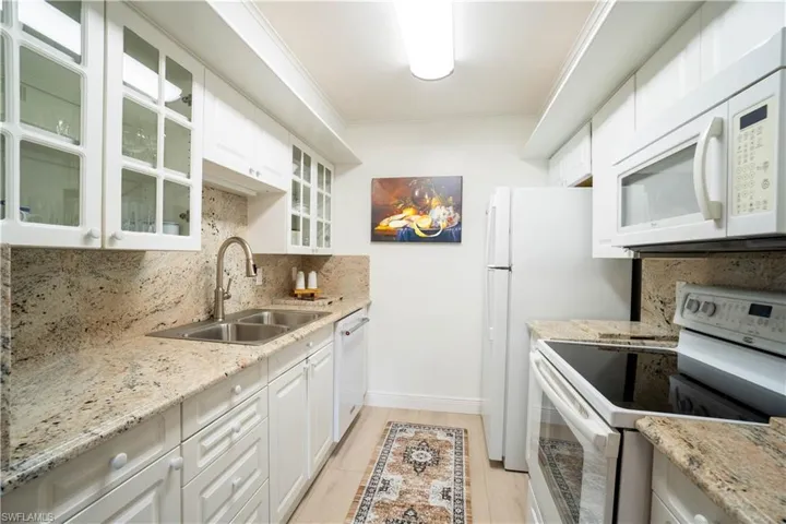 The kitchen features white cabinetry, granite countertops, a double stainless steel sink, and white appliances including a refrigerator, oven, and microwave