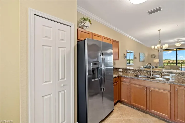 Kitchen featuring stainless steel refrigerator with ice dispenser, a sink, brown cabinets, crown molding, and a chandelier