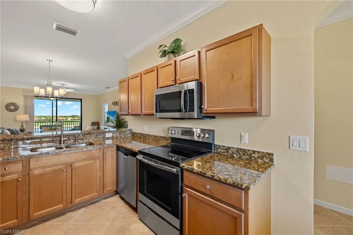 Kitchen with appliances with stainless steel finishes, a sink, ornamental molding, dark stone counters, and a chandelier