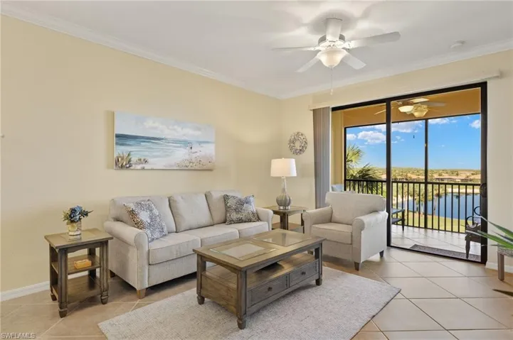 Living room with ceiling fan, light tile patterned flooring, crown molding, baseboards, and a water view