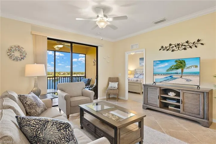Living room with ceiling fan, crown molding, light tile patterned floors, and baseboards