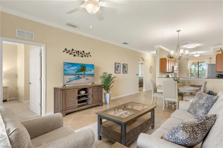 Living room with ornamental molding, arched walkways, a chandelier, a ceiling fan, and baseboards