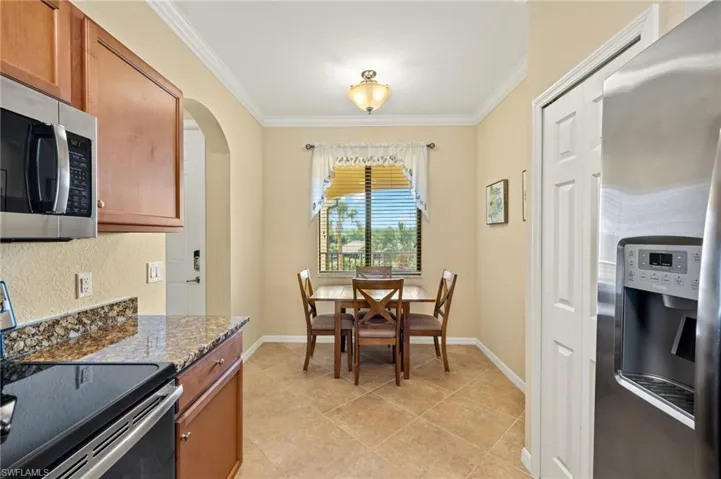 Kitchen with appliances with stainless steel finishes, crown molding, brown cabinetry, dark stone counters, and arched walkways