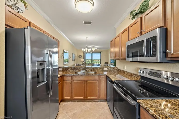 Kitchen with stainless steel appliances, a sink, ornamental molding, brown cabinetry, and light tile patterned floors