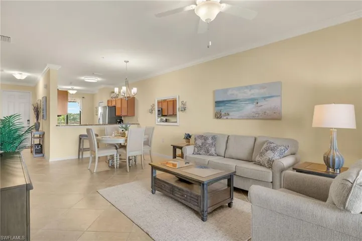 Living room with baseboards, crown molding, light tile patterned flooring, a chandelier, and ceiling fan