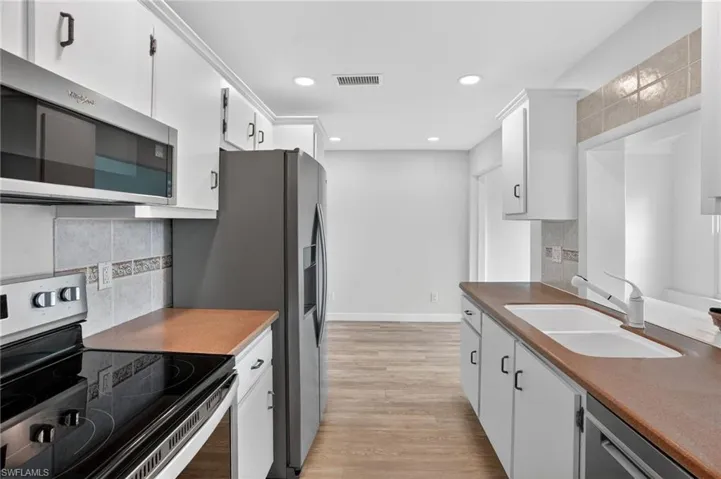 Kitchen featuring stainless steel appliances, tasteful backsplash, white cabinets, light wood finished floors, and recessed lighting