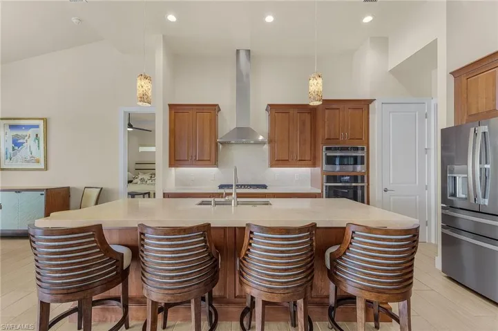 Kitchen with breakfast bar, island with sink, stainless steel appliances, cook top, exhaust hood, tile flooring, and decorative light fixtures
