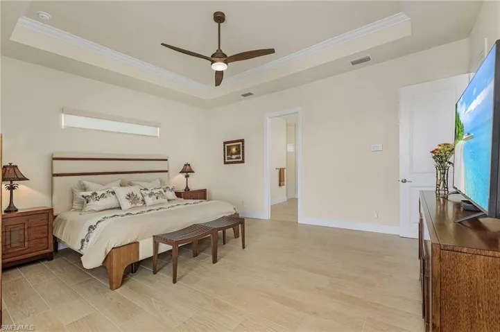 Primary bedroom featuring access to lanai and pool, a view of the canal, tile flooring, a single coffered ceiling with crown molding, and ceiling fan