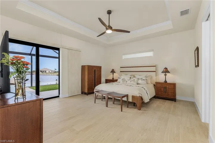 Primary bedroom featuring access to lanai and pool, a view of the canal, tile flooring, a single coffered ceiling with crown molding, and ceiling fan