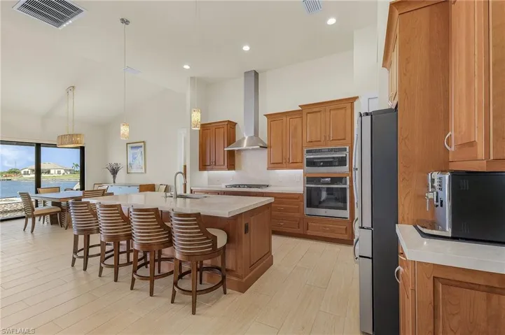 Kitchen with breakfast bar, island with sink, stainless steel appliances, cook top, exhaust hood, tile flooring, and decorative light fixtures