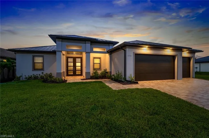 Front exterior featuring a three car garage, the front yard, and paver driveway