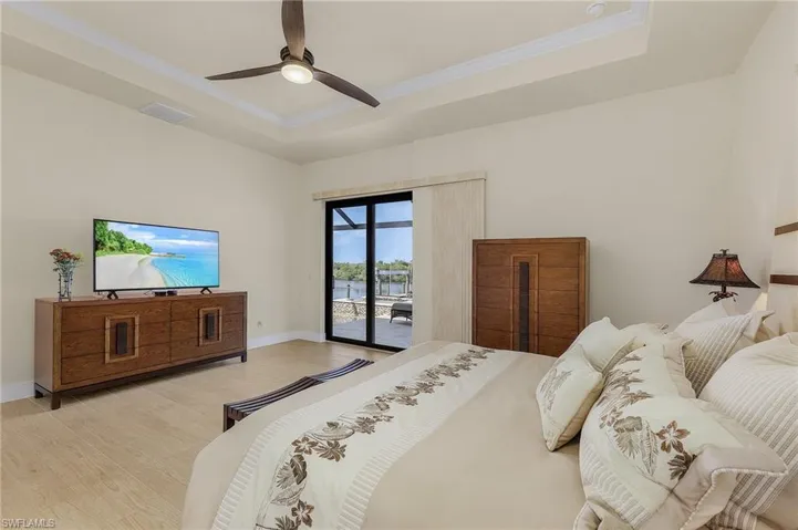 Primary bedroom featuring access to lanai and pool, a view of the canal, tile flooring, a single coffered ceiling with crown molding, and ceiling fan