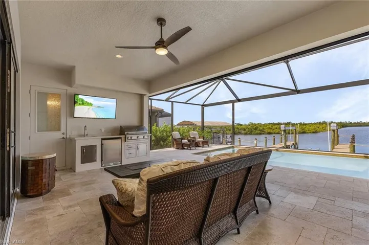 Covered lanai featuring area for grilling, ceiling fan, screened enclosure, and view of canal
