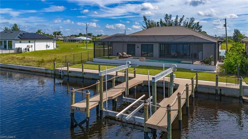 Rear view of property featuring a water view, boat dock and lift, pool and spa, screened enclosure, and fenced in backyard