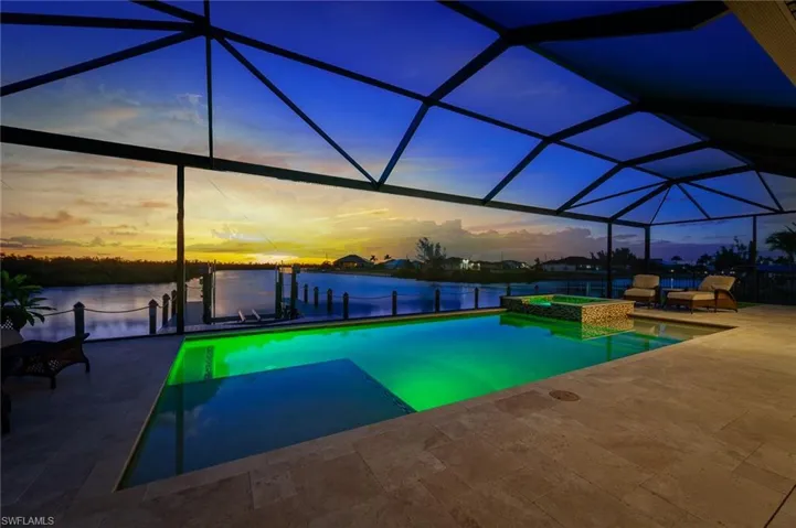 Pool and spa at dusk, screen enclosure, and view of canal