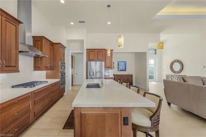 Kitchen with breakfast bar, island with sink, stainless steel appliances, cook top, exhaust hood, tile flooring, and decorative light fixtures