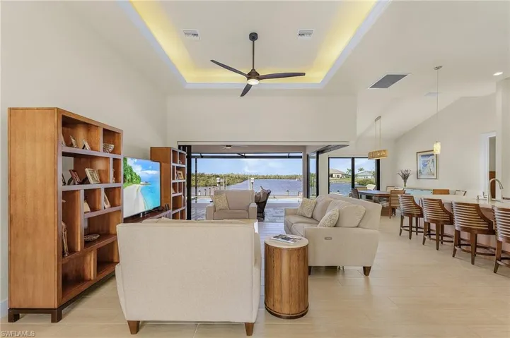 Living room with tile flooring, a single coffered ceiling with crown moulding, ceiling fan, and 90 degree sliders