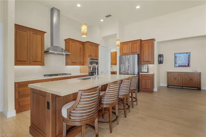 Kitchen with breakfast bar, island with sink, stainless steel appliances, cook top, exhaust hood, tile flooring, and decorative light fixtures