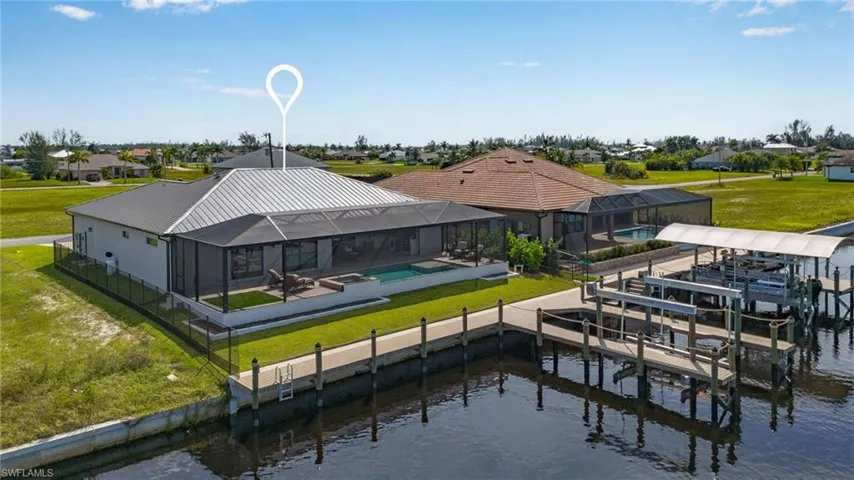 Rear view of property featuring a water view, boat dock and lift, pool and spa, screened enclosure, and fenced in backyard