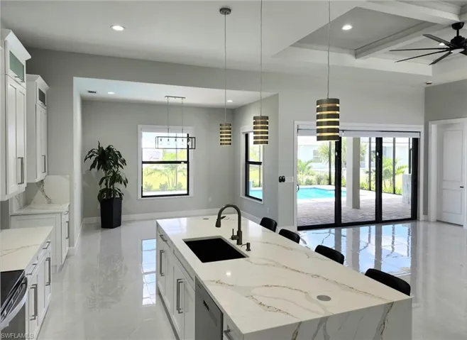 Kitchen with sink, a center island with sink, ceiling fan, and white cabinetry