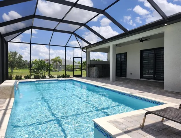 View of swimming pool with pool water feature, ceiling fan, glass enclosure, a bar, and a patio area
