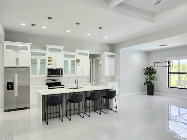 Kitchen with decorative light fixtures, white cabinetry, a kitchen island with sink, and appliances with stainless steel finishes