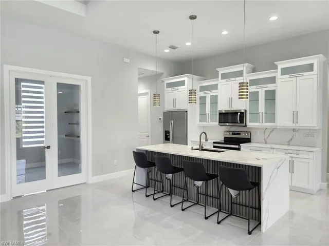 Kitchen with a center island with sink, stainless steel appliances, hanging light fixtures, white cabinets, and backsplash