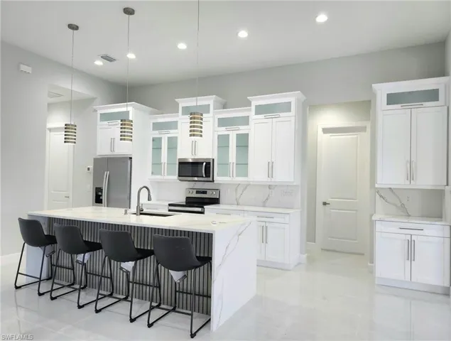 Kitchen featuring hanging light fixtures, a center island with sink, tasteful backsplash, appliances with stainless steel finishes, and sink