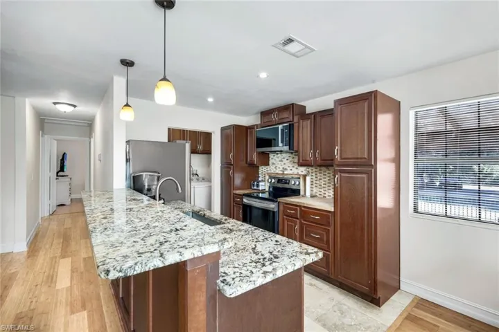 Kitchen with appliances with stainless steel finishes, dark brown cabinetry, hanging light fixtures, light wood-style flooring, and a kitchen breakfast bar
