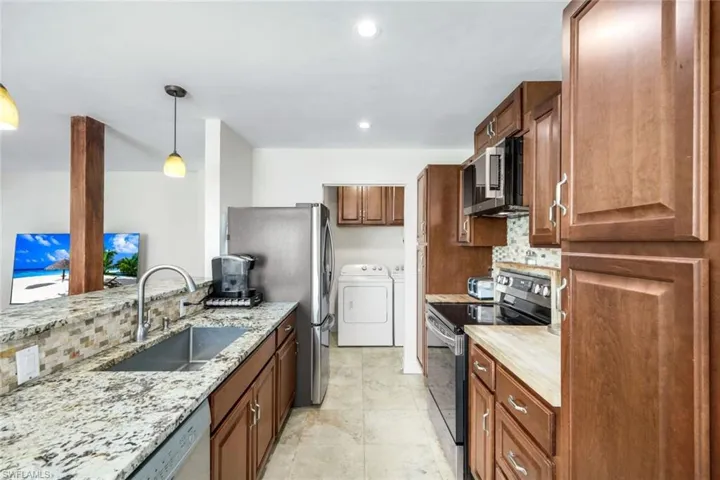 Kitchen with tasteful backsplash, stainless steel appliances, washer and dryer, pendant lighting, and brown cabinetry