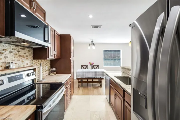 Kitchen with stainless steel appliances, light stone countertops, recessed lighting, decorative light fixtures, and decorative backsplash