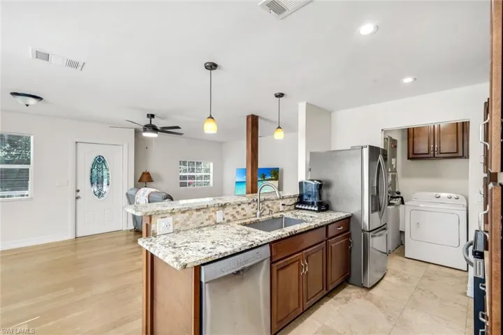 Kitchen featuring decorative light fixtures, appliances with stainless steel finishes, washer / clothes dryer, light stone countertops, and a peninsula