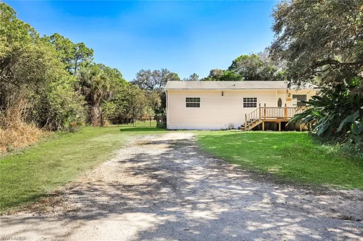 Back of property featuring a wooden deck, a lawn, stairs, and dirt driveway