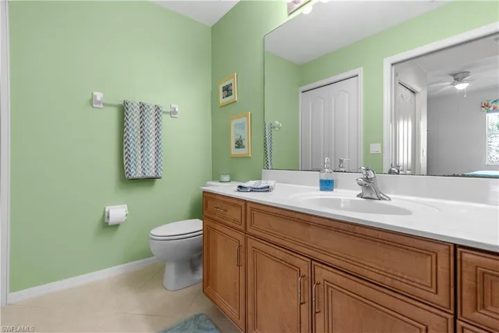 Primary bathroom featuring a wood-finish vanity with a white countertop and integrated sink, a large wall-mounted mirror, and tiled flooring