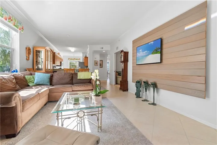 Open-concept living space featuring a wood-panel accent wall with mounted television, crown molding, and large windows