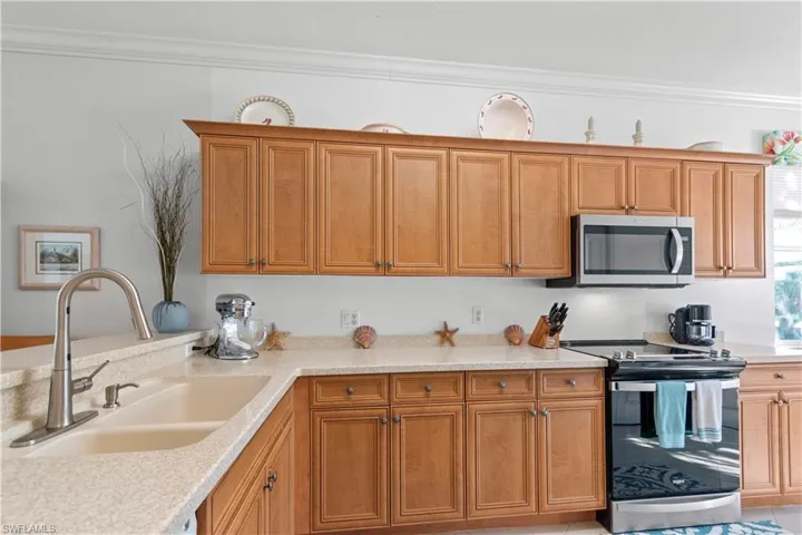 Kitchen featuring wood cabinetry, light-toned countertops, a double basin sink with an arched faucet, a stainless steel over-the-range microwave, and a stainless steel electric range