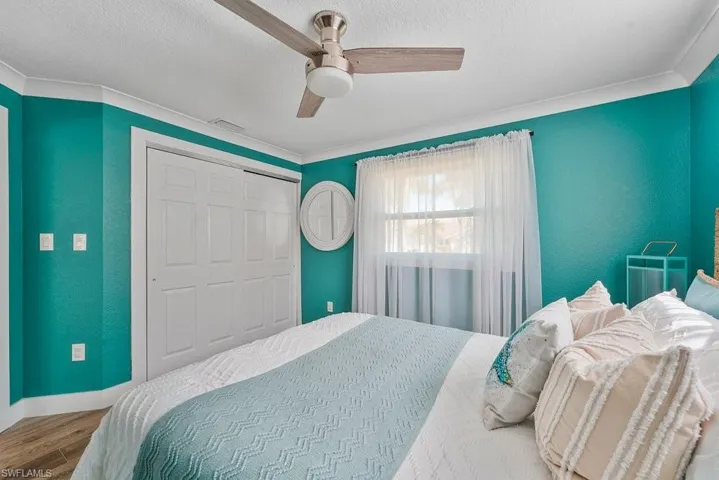 Interior room featuring a ceiling fan, crown molding, wood-finish flooring, sliding closet doors, and a window with sheer curtains