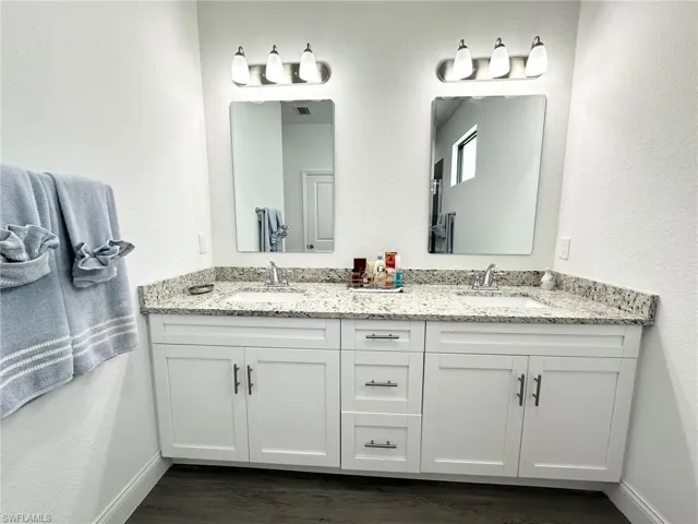 Full bathroom featuring a textured wall, double vanity, and dark wood-style floors