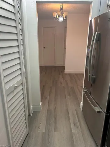 Hallway with a chandelier, light wood-type flooring, and a textured ceiling