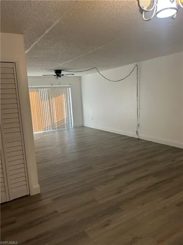 Unfurnished room featuring dark wood-style flooring, a ceiling fan, and a textured ceiling